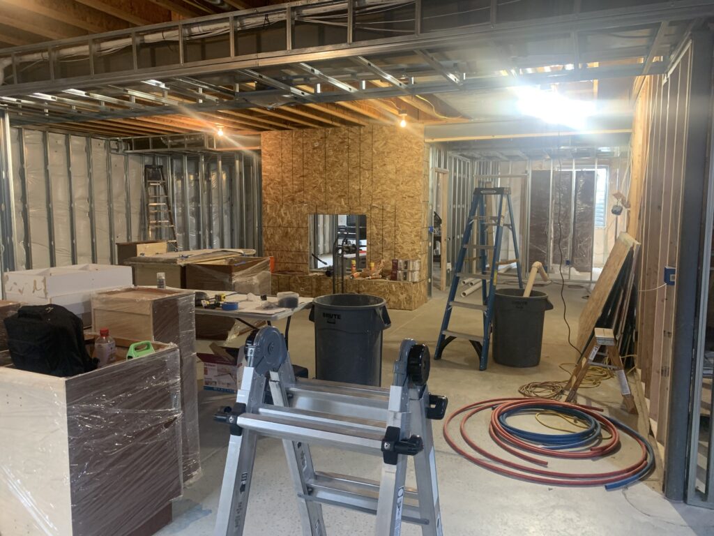 Workers remodel a home, exposing framing and insulation; ladders, tools, cables, and materials fill the IRC-compliant site.