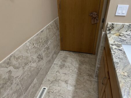 Tan Zellige tiles cover the bathroom corner’s walls and floor. A cloth hangs on the wooden door handle. A sink sits on the right.